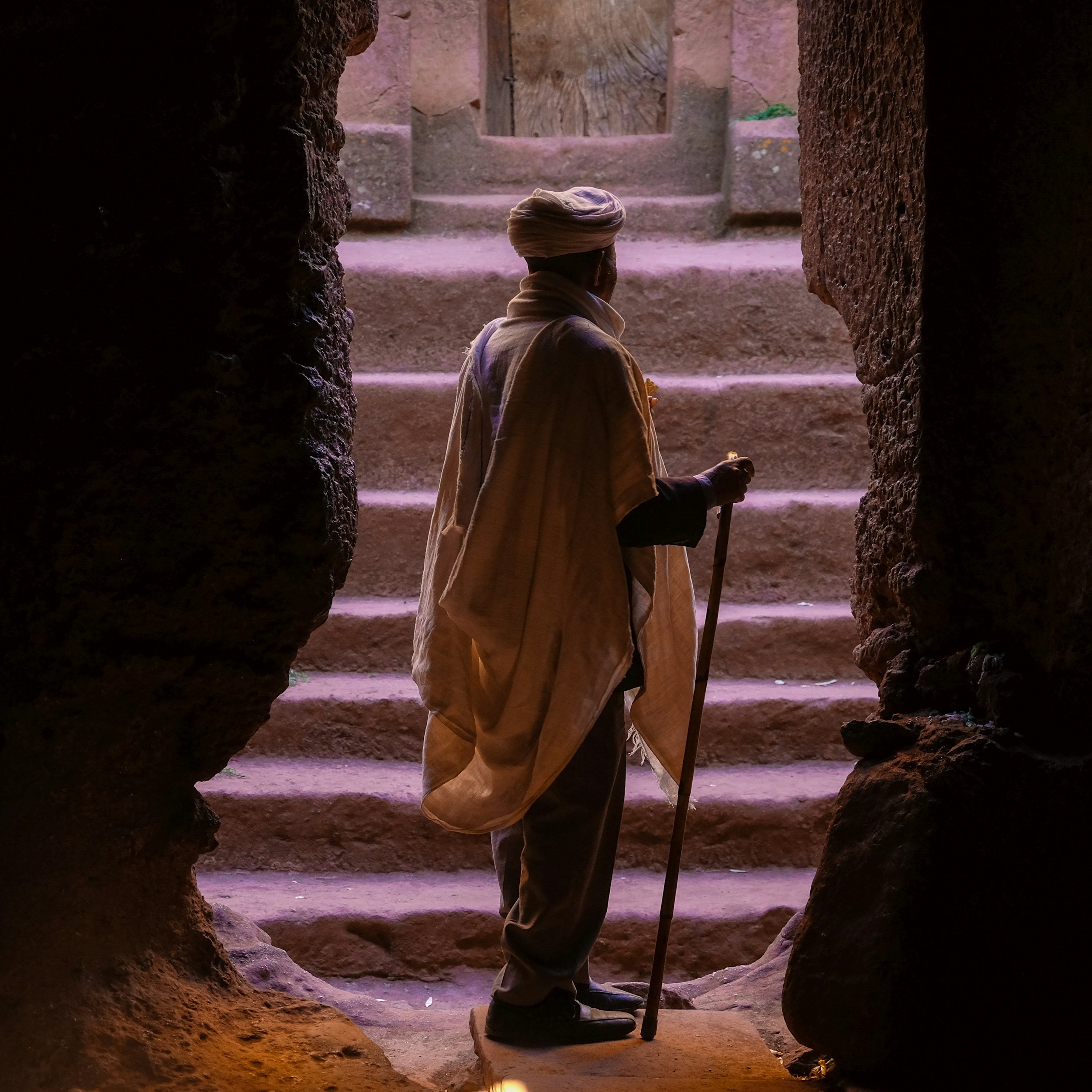 elder with a walking stick by stone stairs